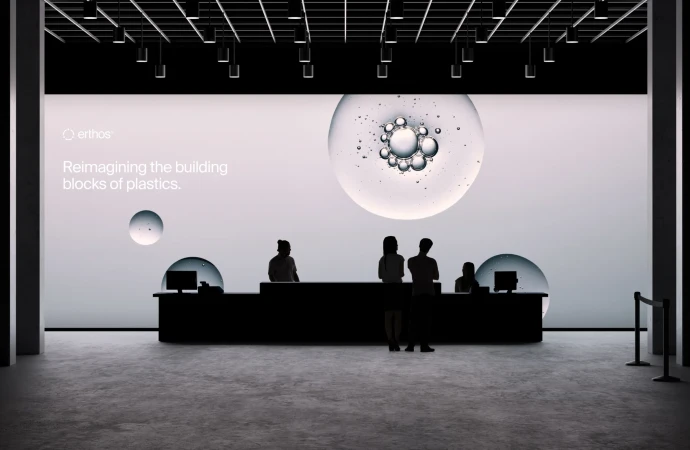 People in silhouette gather at a reception desk in front of a large display featuring molecular graphics and branding in a modern setting.