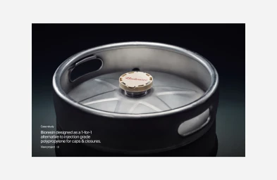 Close-up product shot of a metallic beer keg featuring a branded beige cap on a dark gradient background with reflective surface.