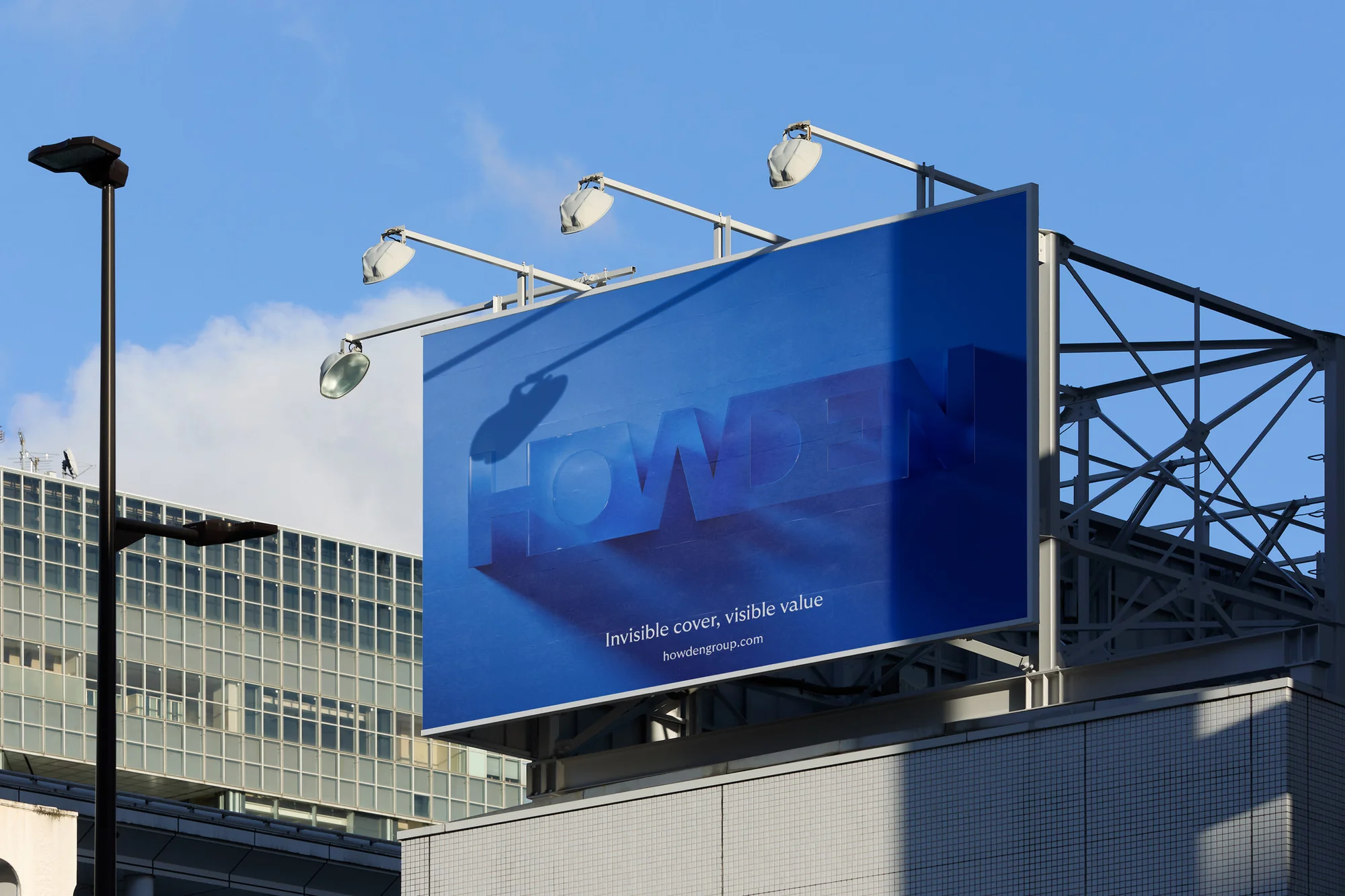 Billboard advertisement for Howden Group against blue sky and buildings. Text reads: Invisible cover, visible value, howdengroup.com