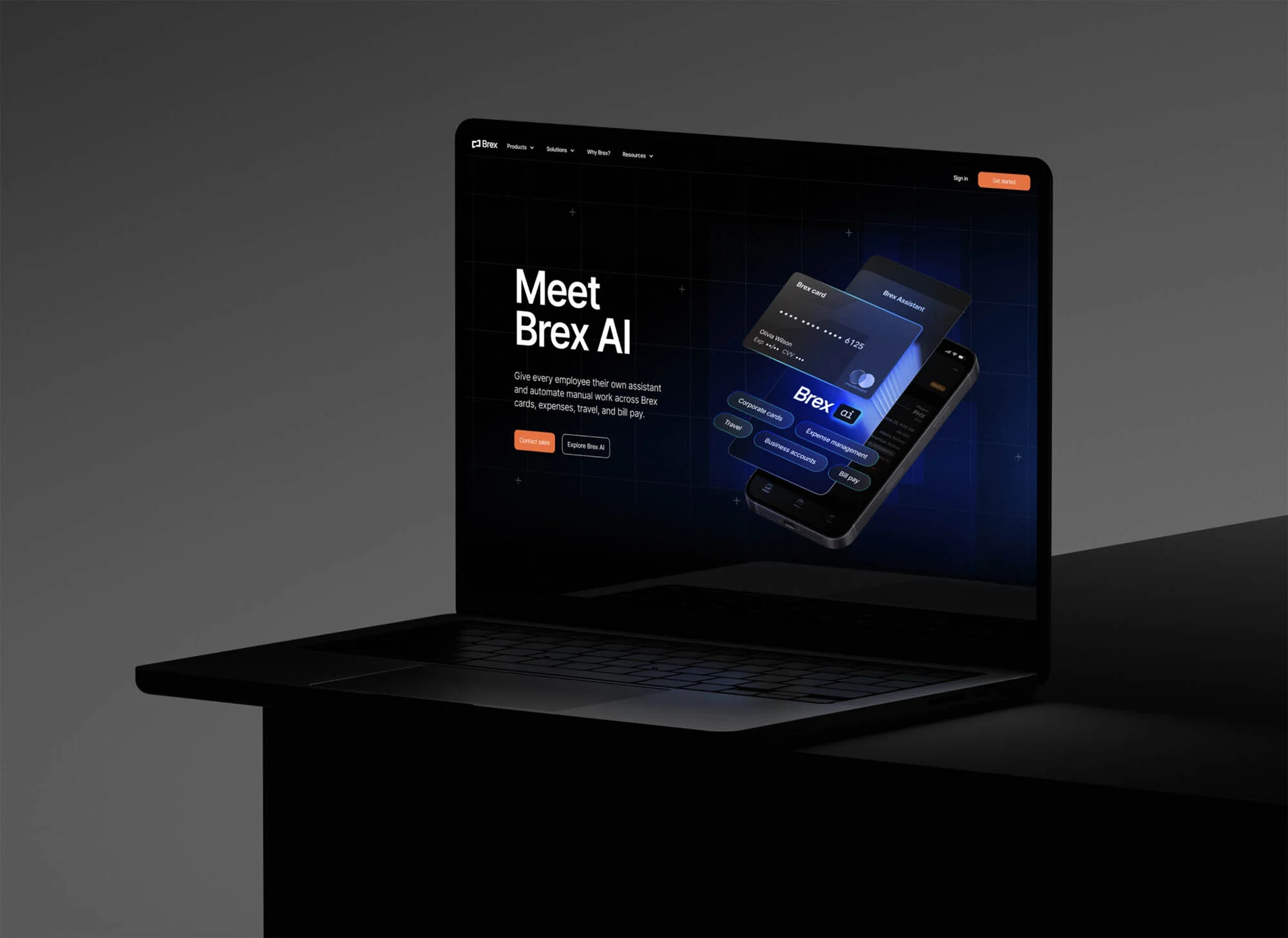 Laptop displaying Brex AI interface with credit cards and mobile integration, illuminated by soft lighting against a dark grey backdrop.