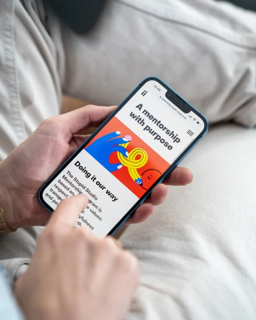 Close-up of a person holding a smartphone displaying a colorful website design with text and graphic elements, neutral-toned background.
