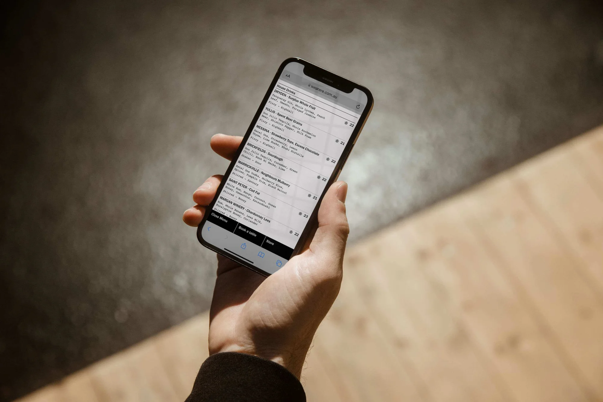 Close-up of a person holding a smartphone displaying a list, illuminated by natural light creating shadows on the phone and hand.