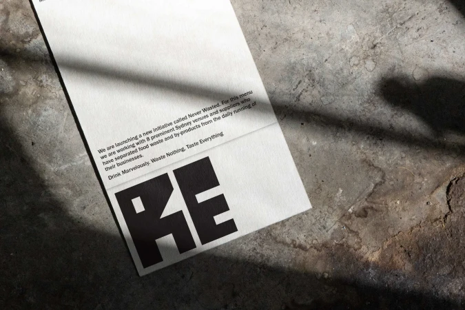 Close-up of a menu on a concrete surface, featuring text about sustainability and bold black letters that spell out RE.