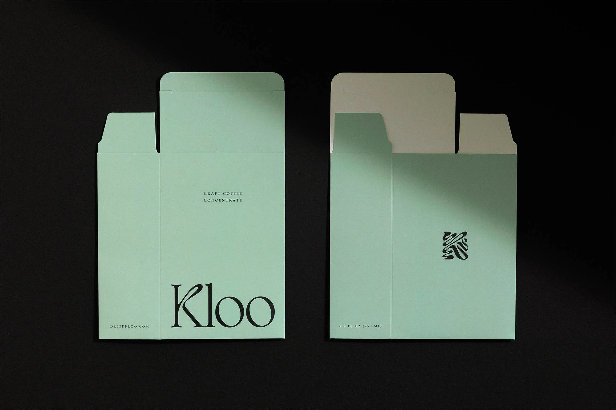 Two light green cartons of Kloo craft coffee concentrate, one opened, sitting on a black surface in a studio product shot.
