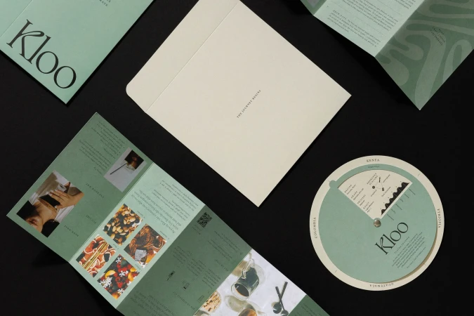 Overhead shot of Kloo brand marketing materials including brochures, a circular guide, and an envelope on a black background.
