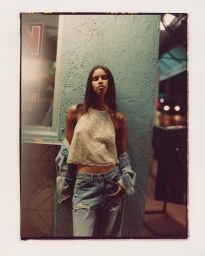 Model leaning against a turquoise wall wearing a beaded halter top and distressed denim jeans for Anthropologie.
