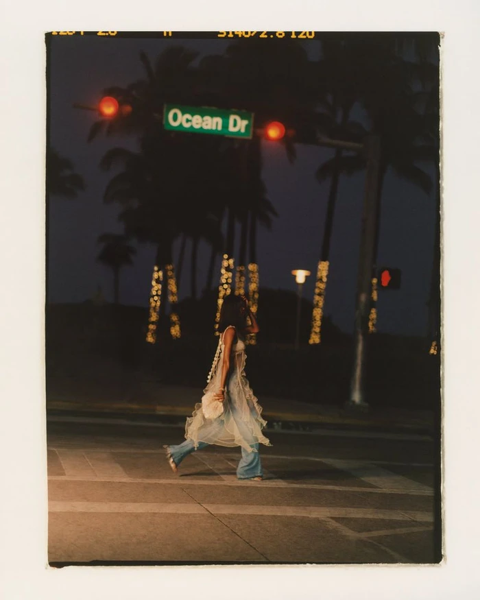 Model Daiane Sodre crossing an illuminated street at night under an Ocean Dr street sign for Anthropologie Spring Catalog