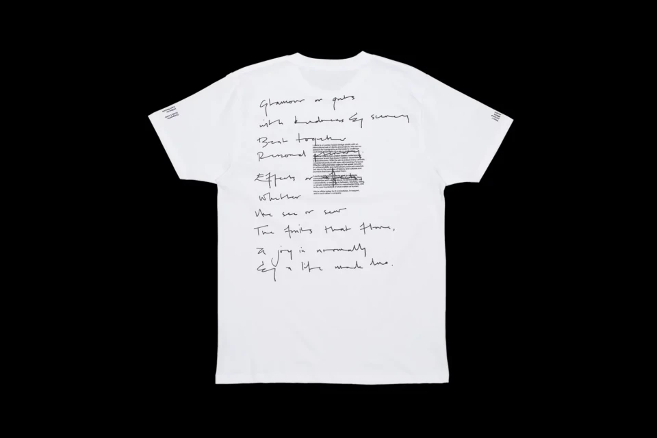 White t-shirt on a black background featuring black handwritten script. The focus is on the rear of the t-shirt and the calligraphic design.