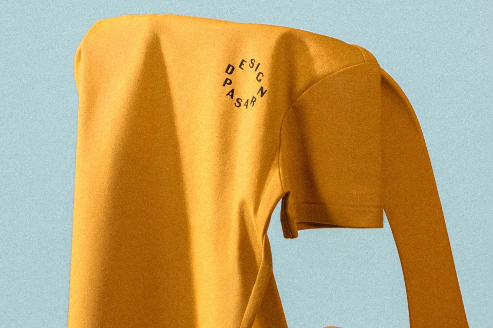 Yellow long-sleeved shirt with a printed logo on a blue background, showcasing minimalist fashion and branding elements.