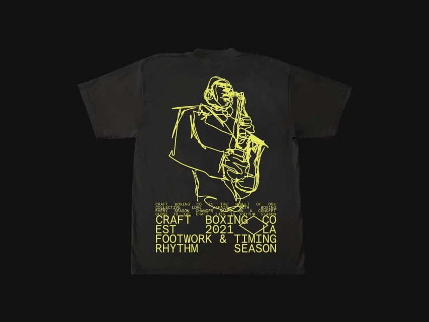Black t-shirt featuring a yellow line art graphic of a musician playing a saxophone and yellow block text on a dark background.