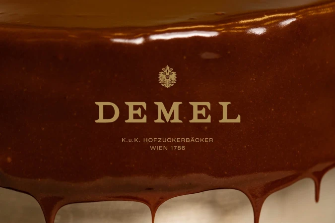 Close-up of glistening brown chocolate coating over pastry with the Demel logo, from the famous Viennese confectionery company.