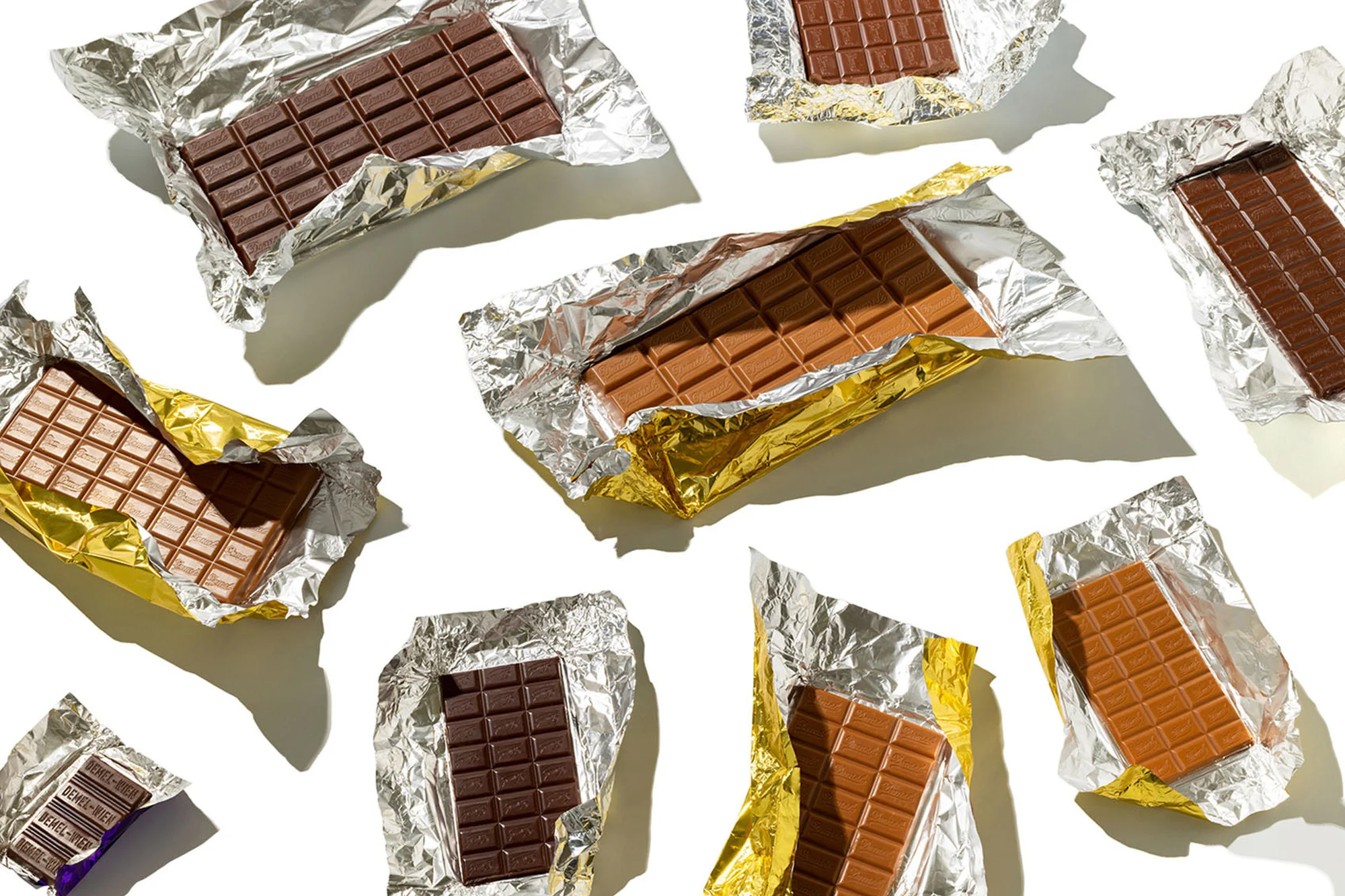 Overhead shot of multiple chocolate bars in foil wrappers, with some bars milk chocolate and others dark chocolate, on a white surface.