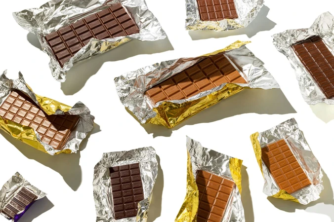 Overhead shot of multiple chocolate bars in foil wrappers, with some bars milk chocolate and others dark chocolate, on a white surface.
