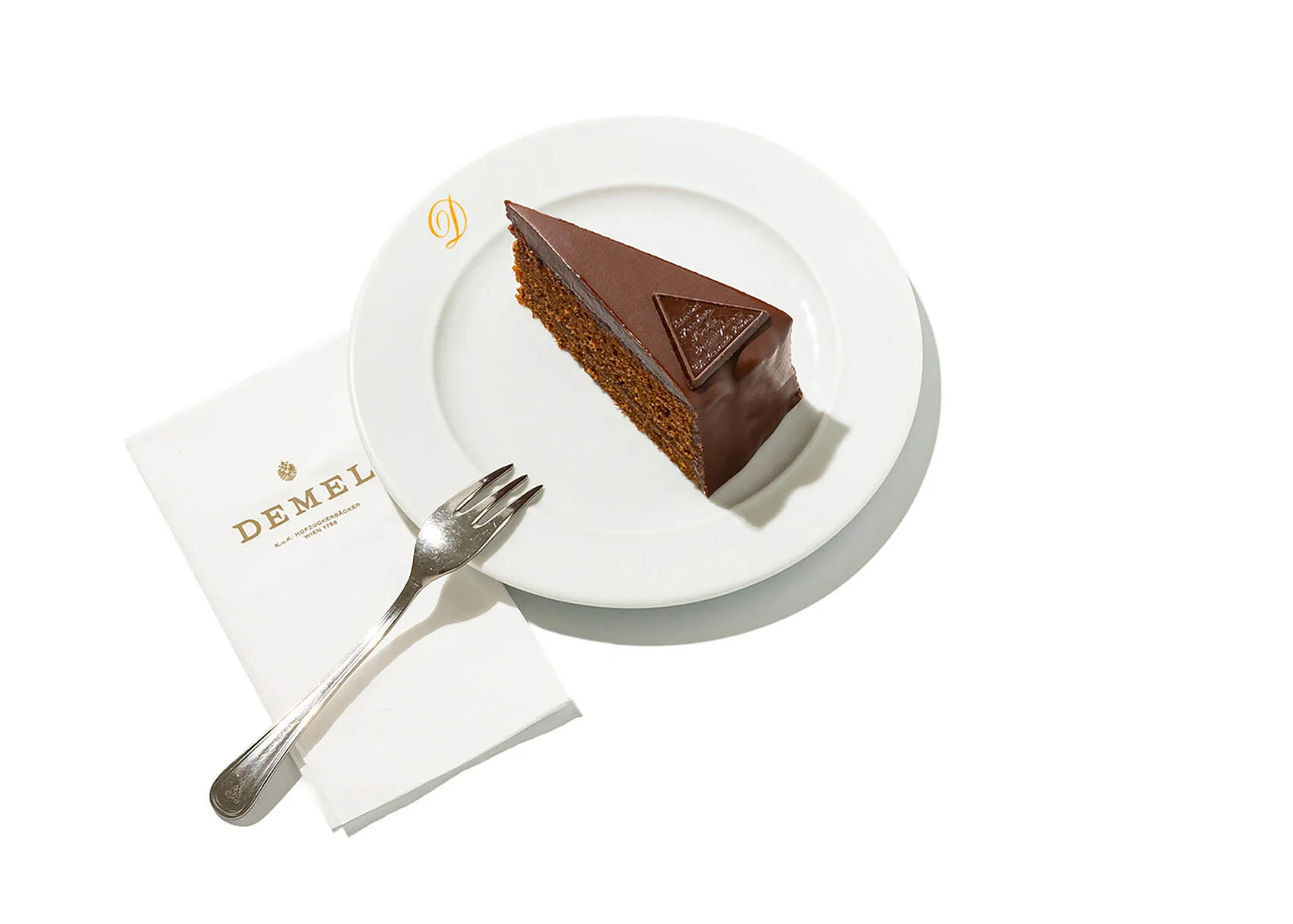Slice of Sachertorte on a white plate with a fork and Demel napkin, studio lighting, food photography, elegant presentation.
