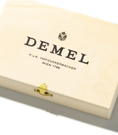 Wooden box with printed Demel brand typography and a gold metal latch on a white surface