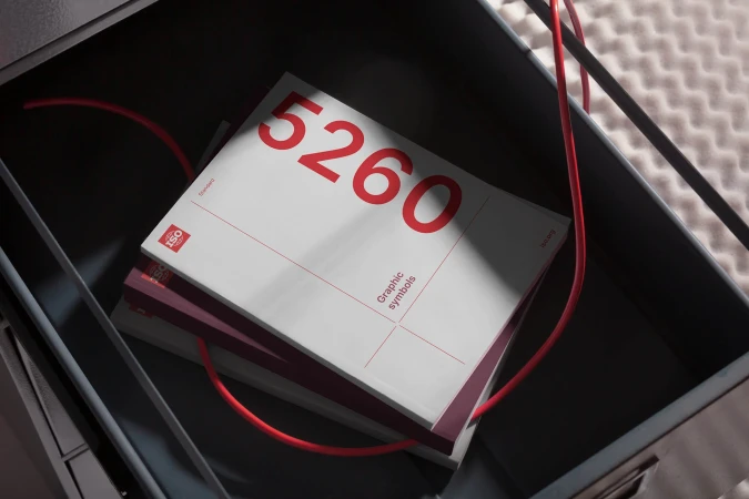 Stack of graphic symbol books with red number 5260, inside a metal container with a red wire.