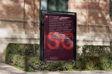 ISO brand identity sign displayed outdoors in front of a brick building with trimmed hedges and gravel ground