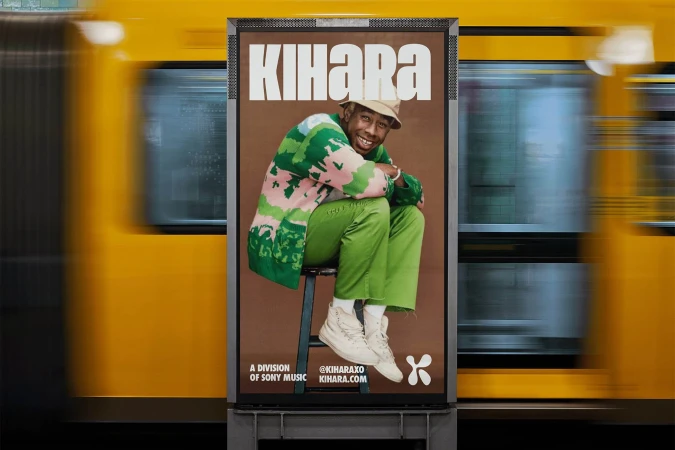Poster featuring a person in green sweater and pants sitting on a stool, with the word KIHARA above them, next to a passing train.