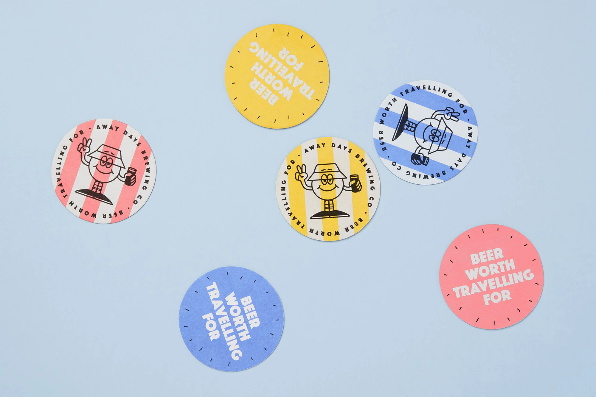 Overhead shot of colorful round coasters with cartoon figures and the text 'Beer Worth Travelling For' against a blue background.