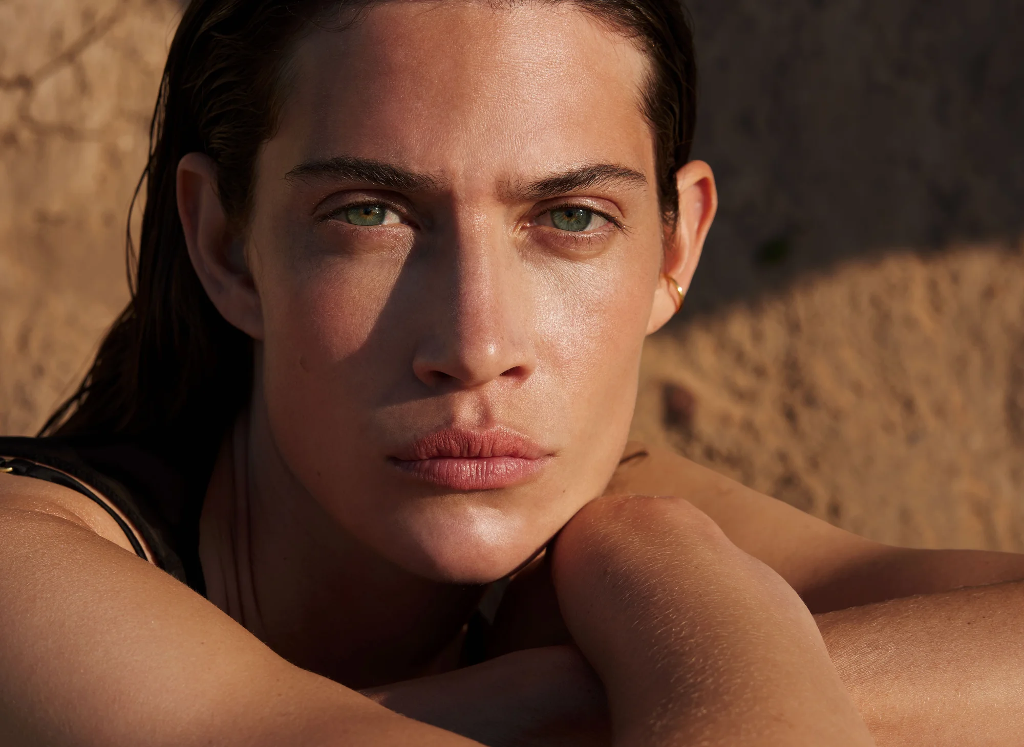 Close-up portrait of a woman with green eyes and wet hair. She is in a natural outdoor setting with soft, warm lighting.