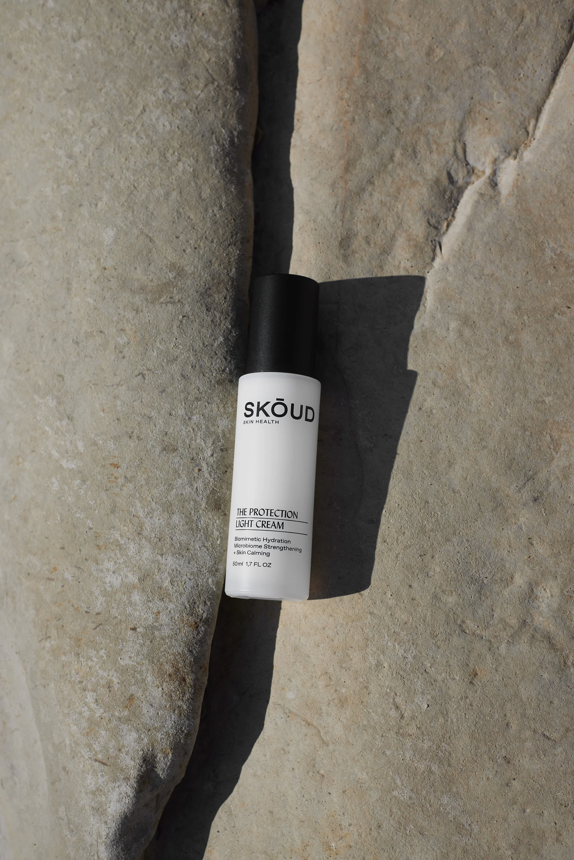 Skoud Australia product shot of The Protection Light Cream bottle with black cap against a textured rock surface in natural light.