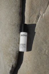 SKOUD Cosmetics bottle resting in a crevice between rough stone surfaces under natural sunlight