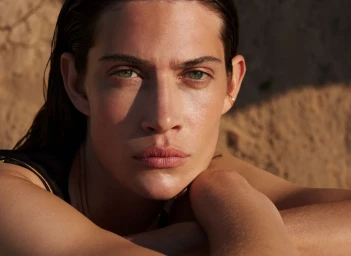 Close-up portrait of a woman with wet hair resting her chin on her crossed arms outdoors in natural sunlight.