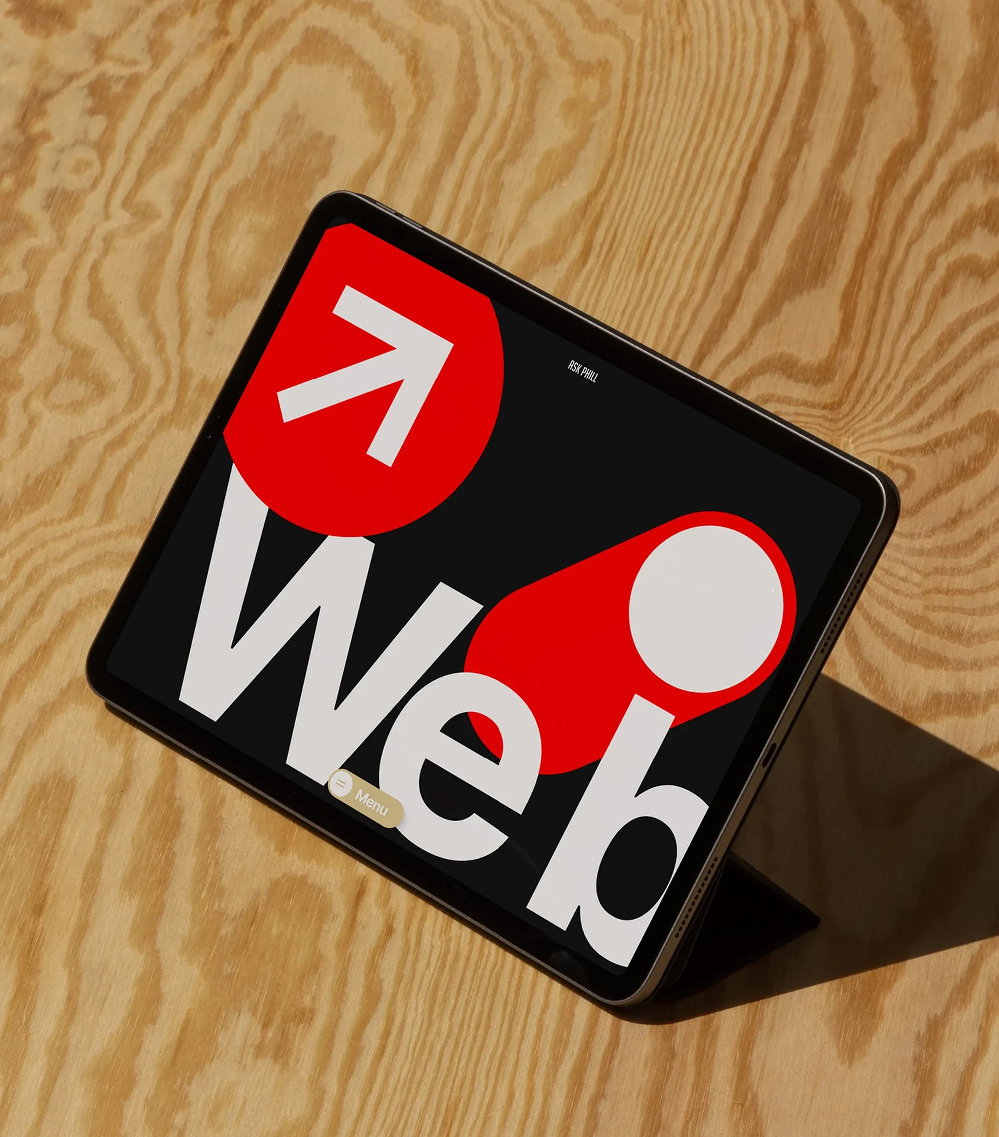 Modern tablet displaying Web design with graphic elements in red, white, and black on a light wood surface, angled view.