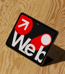 Tablet angled on wooden surface displaying graphic design interface with bold red and white branding elements