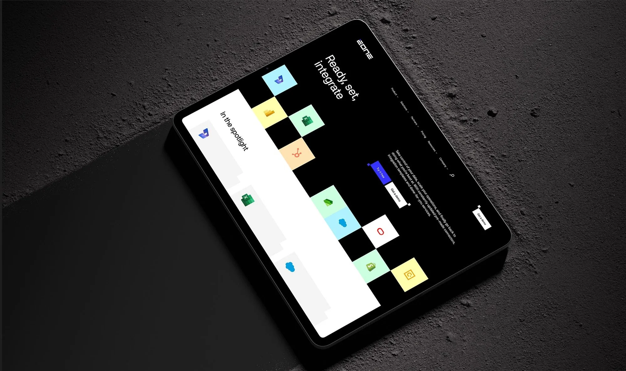 Digital tablet displays a sleek, modern website interface with a black background and vibrant icons, set against a dark concrete surface.