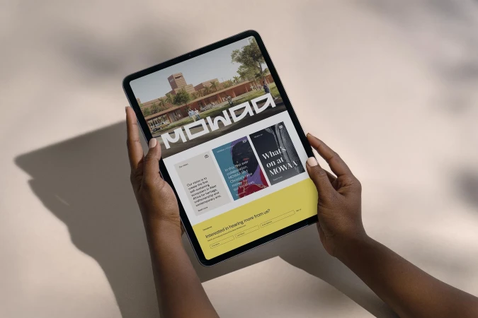 Person holds a tablet displaying the MOWAA website, showcasing architecture and contemporary art. The interface features navigation and highlights.