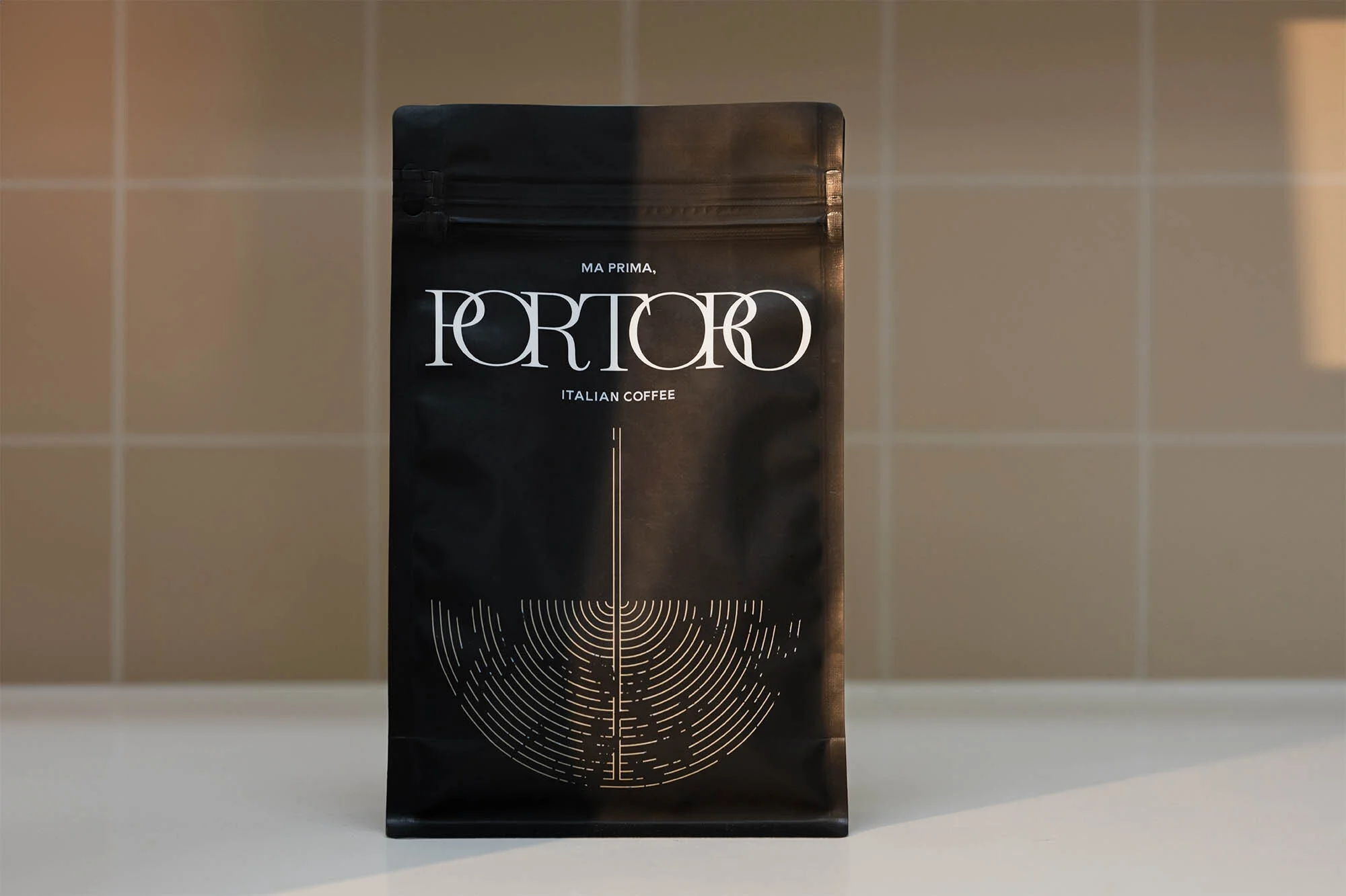 Close-up of a black bag of Portoro Italian Coffee with white text and graphic design on a white surface with a light brown tiled background.