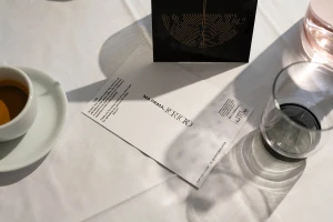 Overhead shot of Portoro coffee brand stationery, espresso cup, and glass on a white tablecloth under natural light.