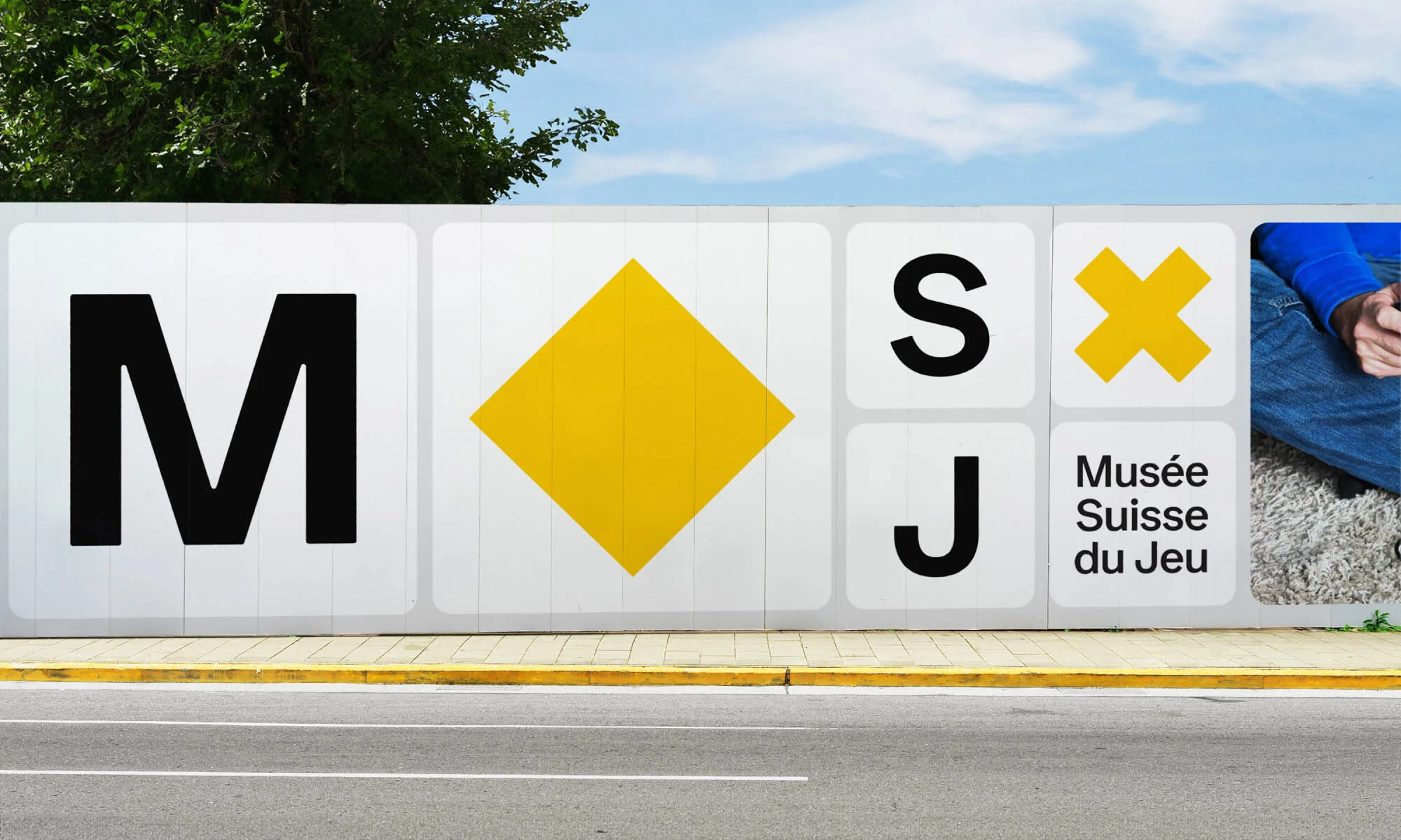 Outdoor advertising billboard featuring black letters 'M, S, J' and a yellow diamond and cross, with 'Musée Suisse du Jeu' text.