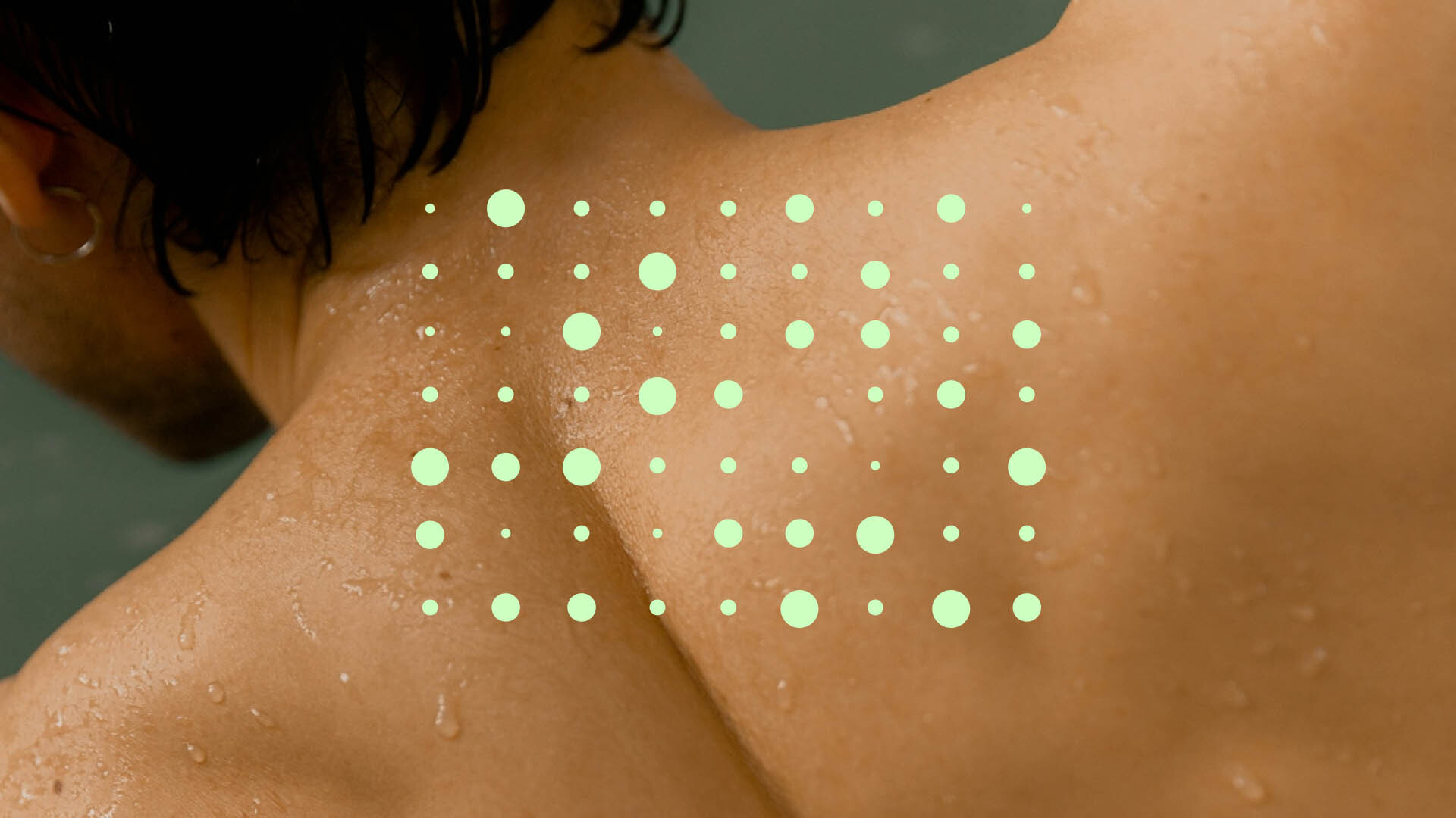 Close-up of a person's upper back and neck, with water droplets and a pattern of light green translucent circles overlaying the skin.
