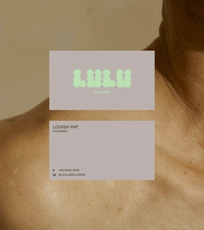 Two business cards on a person's shoulder. The cards feature the brand name LULU WELLNESS in green and contact information.