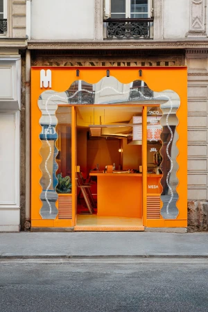 Bright orange exterior of a 'Mesa' taco restaurant in a city setting, featuring a wavy mirror facade and urban street view.