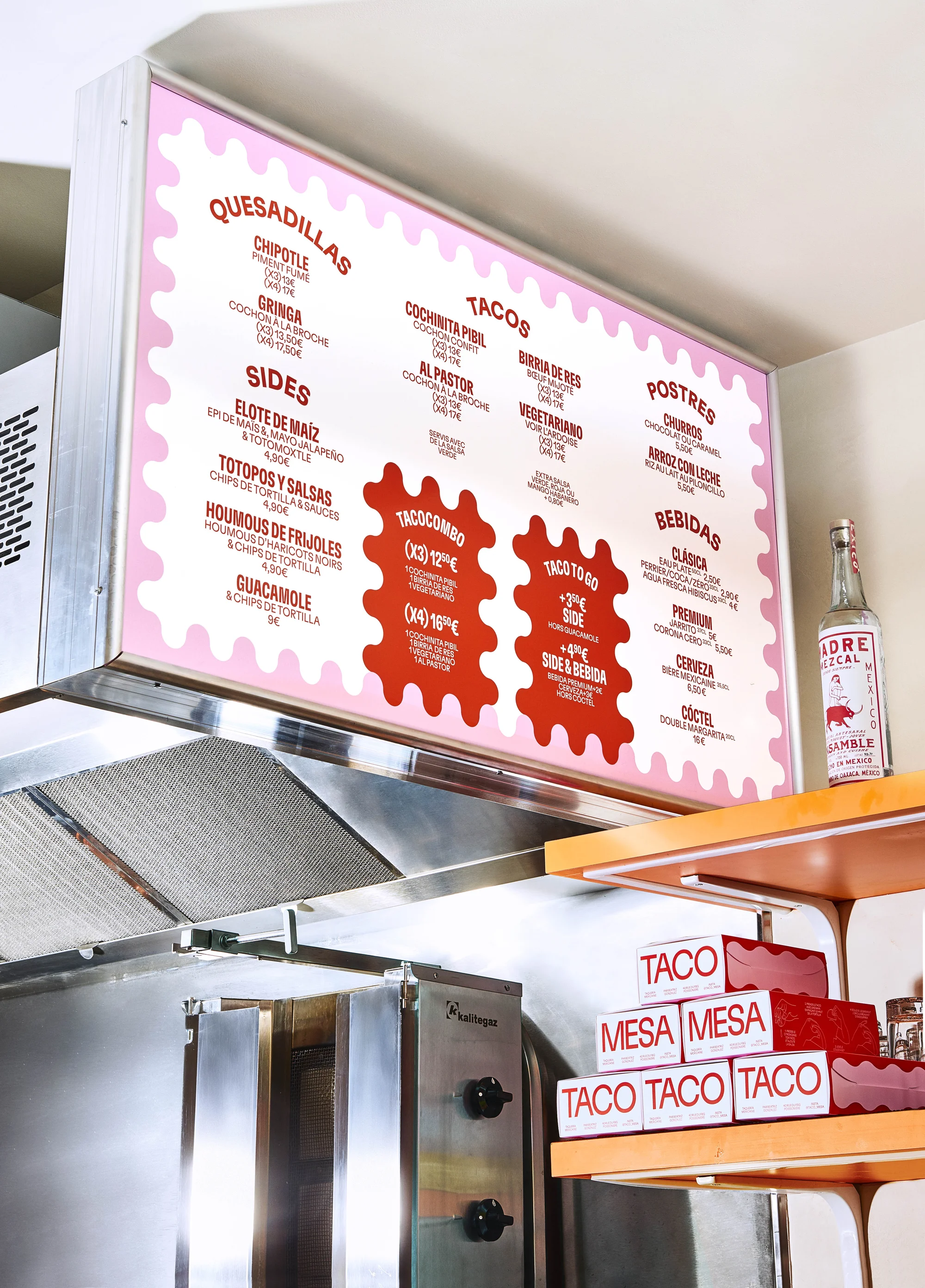 Overhead shot of a restaurant menu board with a pink border displaying Mexican food items such as tacos and quesadillas.