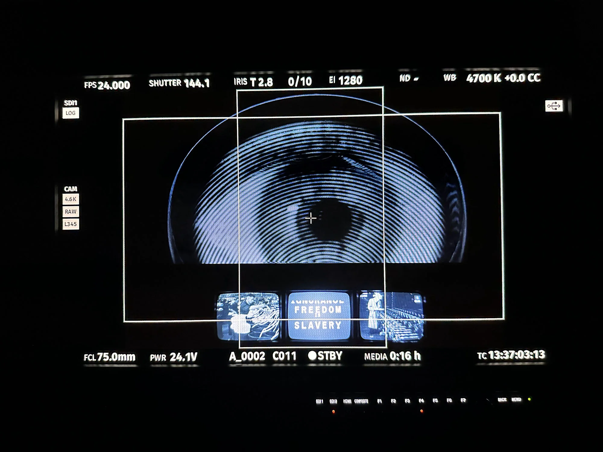 Close-up of a video monitor displaying an eye with concentric circles; technical data, film settings, and the words 'Freedom' and 'Slavery'.