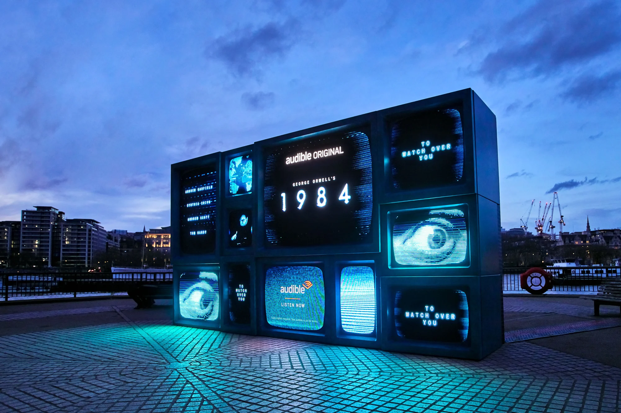Outdoor art installation featuring stacked vintage TV sets displaying imagery and text related to George Orwell's '1984' and Audible.