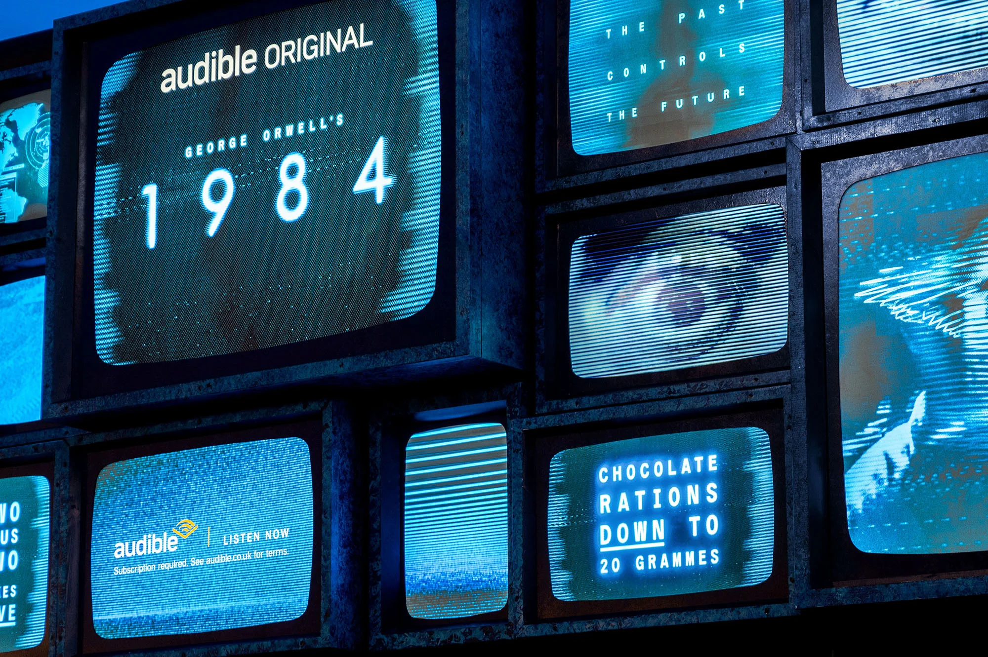 A collection of vintage TV screens displaying audio-visual content: the title of George Orwell's 1984, an eye, and the Audible logo.