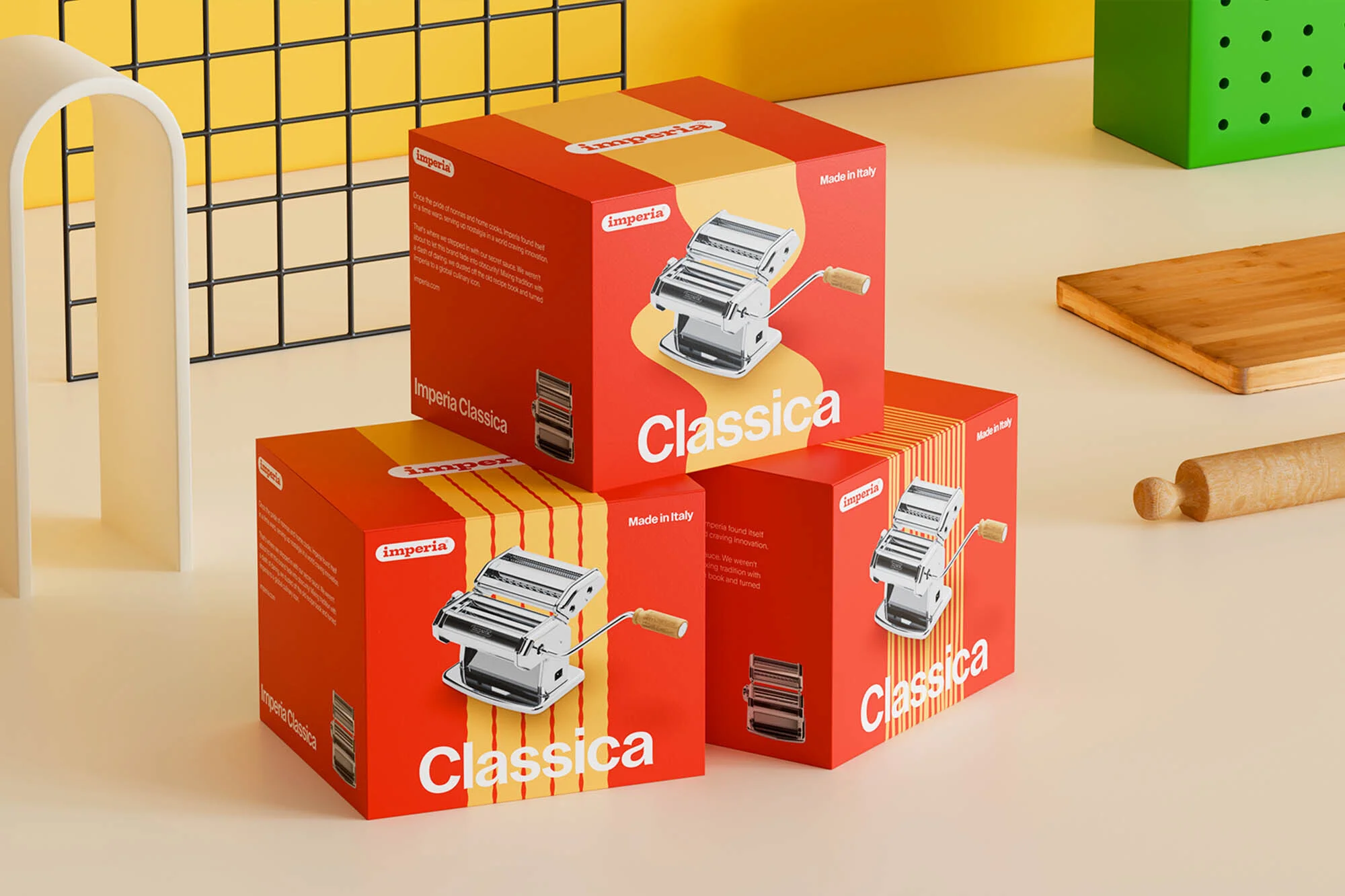 Three Imperia Classica pasta machine boxes stacked, featuring product images, against a yellow and beige backdrop with kitchen props.