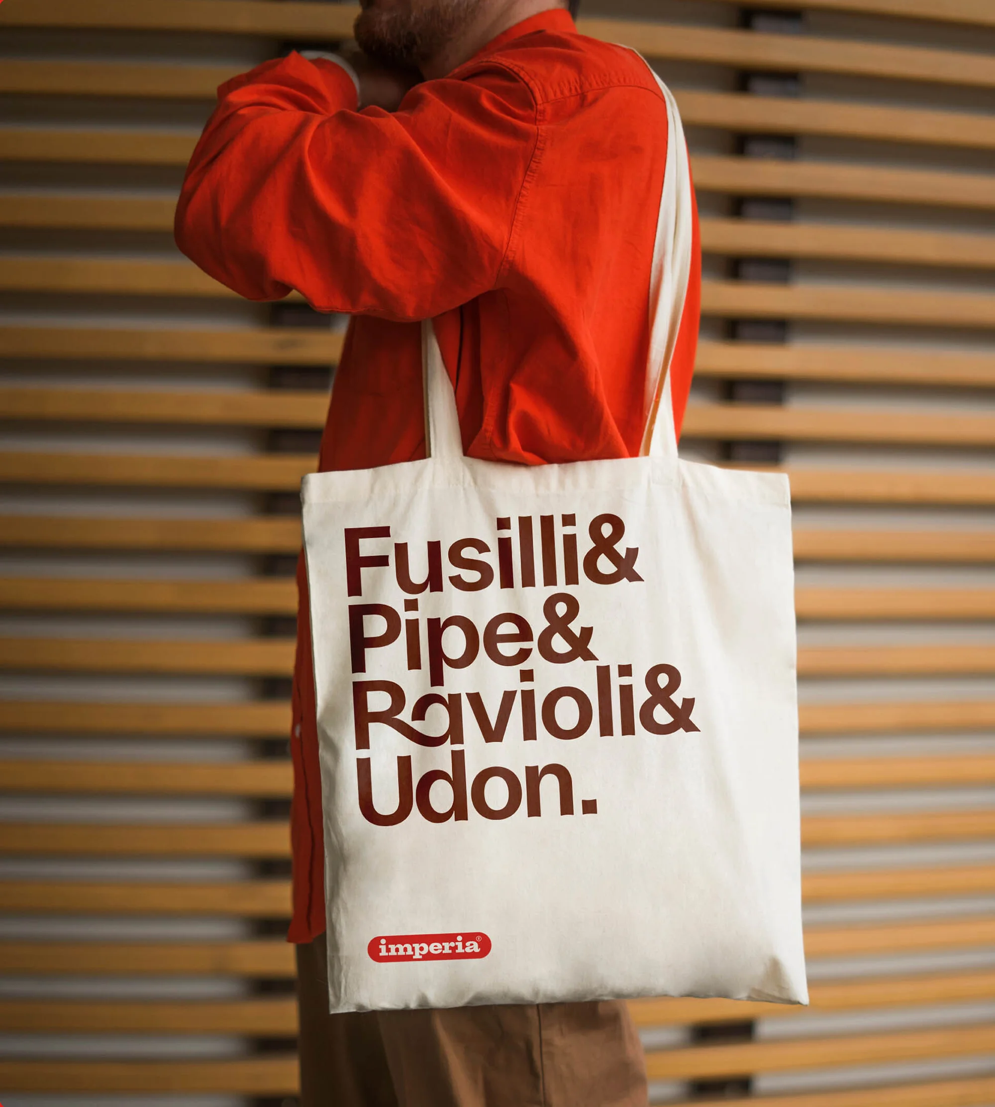 Person wearing orange shirt carrying a white tote bag with pasta names printed in brown and Imperia logo visible on the lower section.