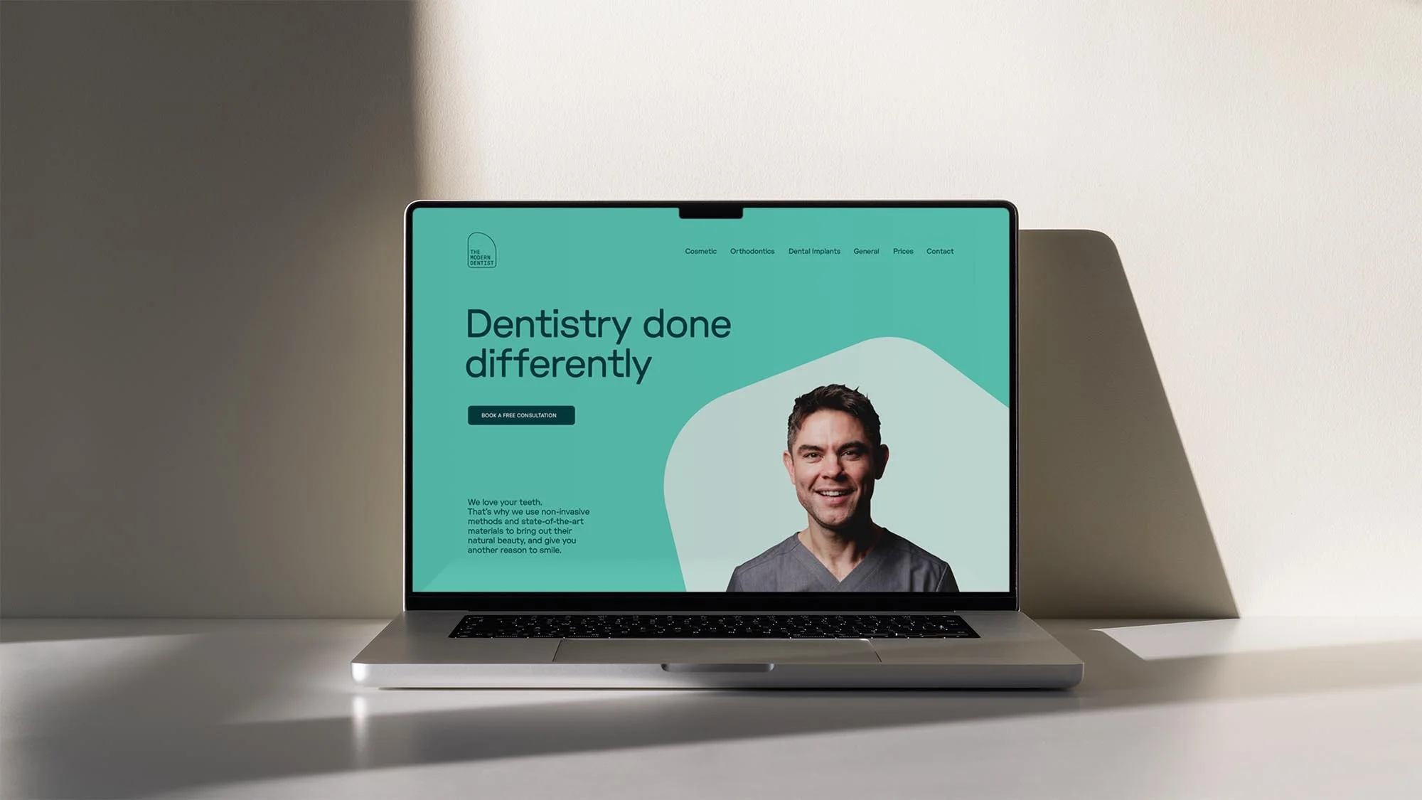 Laptop displaying dentistry website with a smiling man, mint green background, and clean design, set against a neutral backdrop.