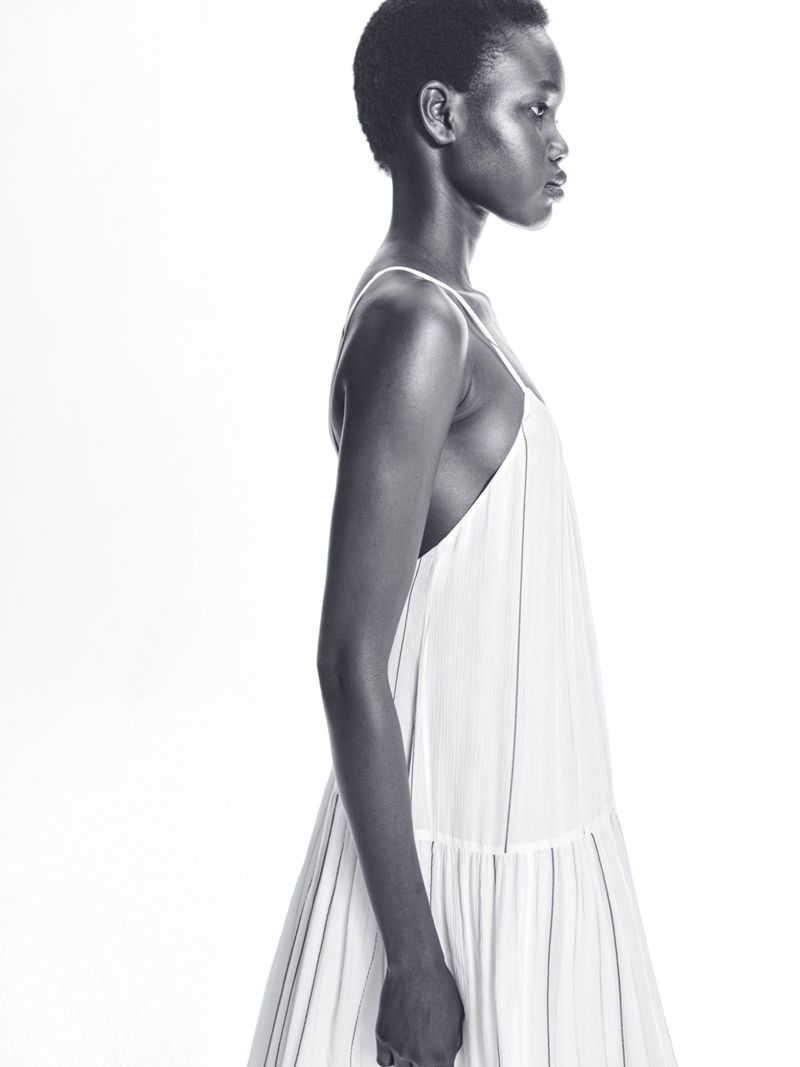 Side profile of a Black woman wearing a white dress against a bright white backdrop, minimalist studio aesthetic, fashion-forward.
