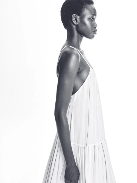 Side profile of a Black woman wearing a white dress against a bright white backdrop, minimalist studio aesthetic, fashion-forward.