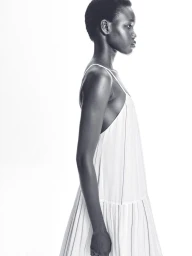 Profile portrait of a Black female model wearing a white slip dress against a seamless white background.