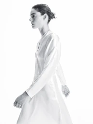 Model in a white long-sleeve dress walking against a bright seamless white background