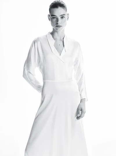 Model wearing a white silk V-neck dress standing against a plain white studio background