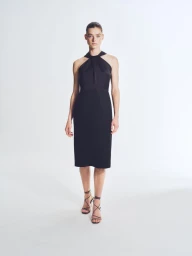 Model standing on a white background wearing a black halter dress and strappy sandals for the BOSS SU25 collection.